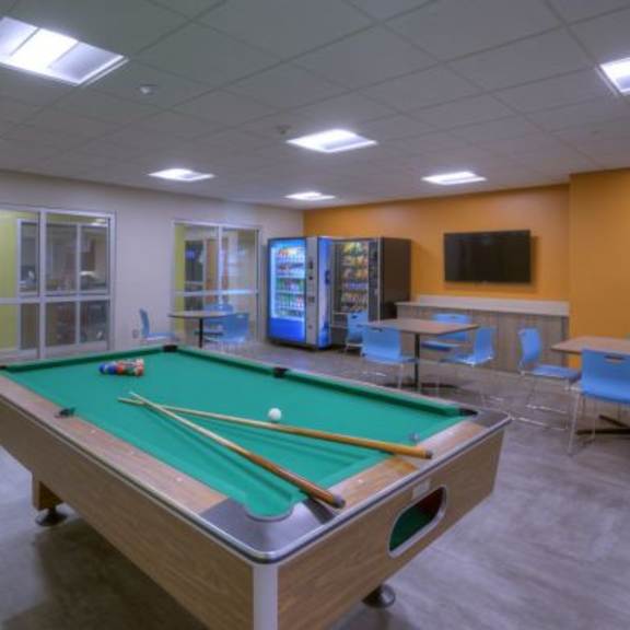 a pool table is in the middle of a room with chairs and a television.