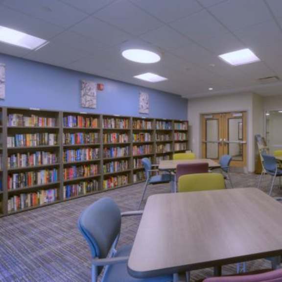 a library with a table and chairs in the foreground and bookshelves in the background.