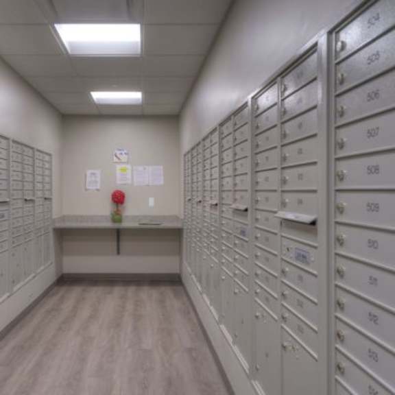 a long hallway with a row of mailboxes on the right and a red flower on the wall.