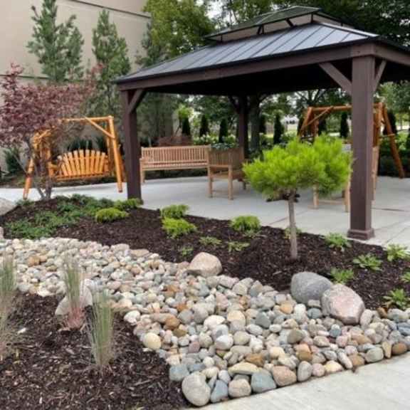 a gazebo is surrounded by a rock garden and a wooden bench.
