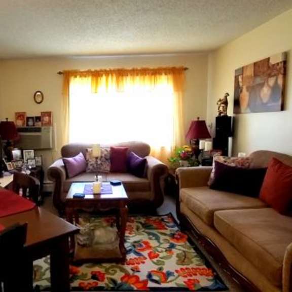 a living room with a brown couch, a red table, and a vase of flowers.