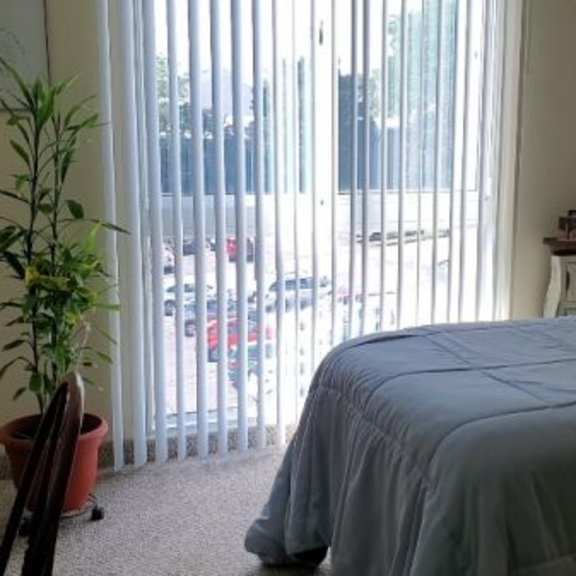a bedroom with a bed, nightstand, and window with blinds.
