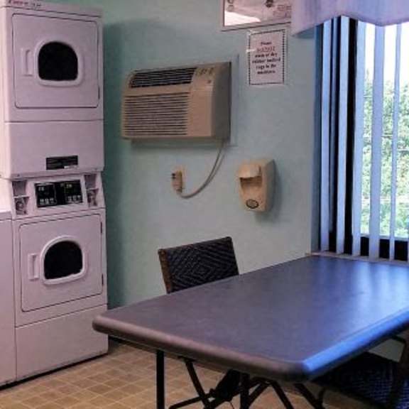 a stack of white washing machines in a room with a table and chairs.