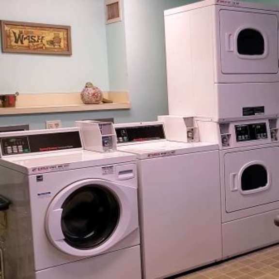a stack of white washing machines in a room with a table and chairs.