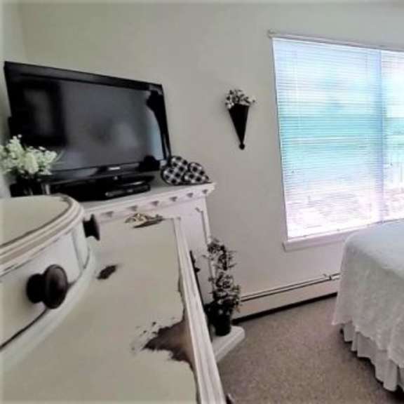 a white bedroom with a bed, dresser, and window.