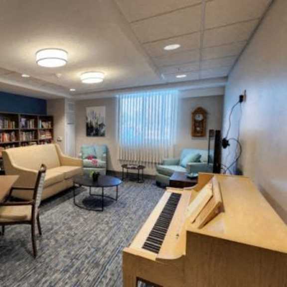 a room with a piano, chairs, and bookshelves.