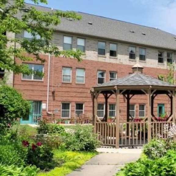 a gazebo is surrounded by flowers in a courtyard between two red brick buildings.