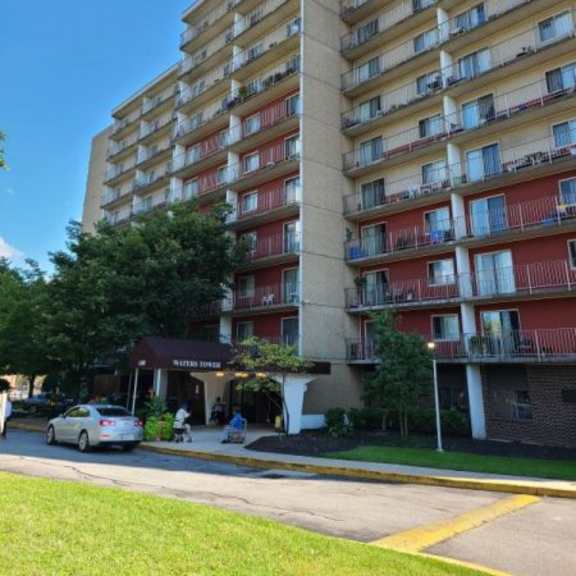 a tall apartment building with a red awning and a car parked in front.