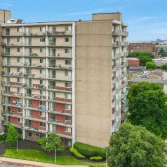 a tall residential building with balconies and a green lawn in front.