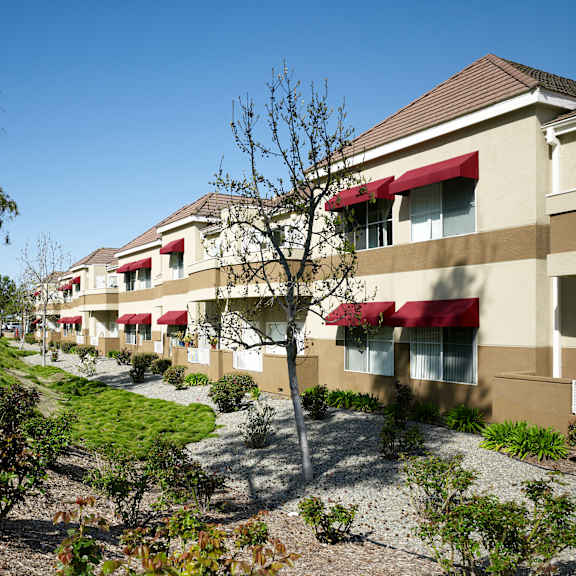 a row of apartment buildings with red awnings and green bushes in front.