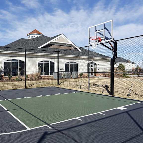 a basketball court is surrounded by a fence and a house is in the background.