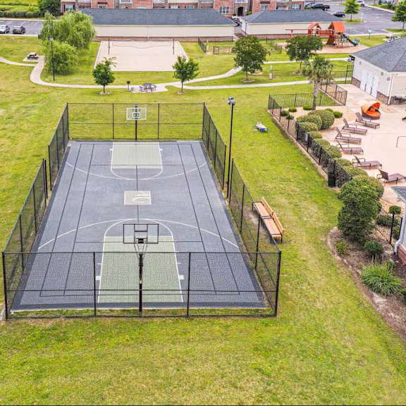 a basketball court is surrounded by a green fence and grass.