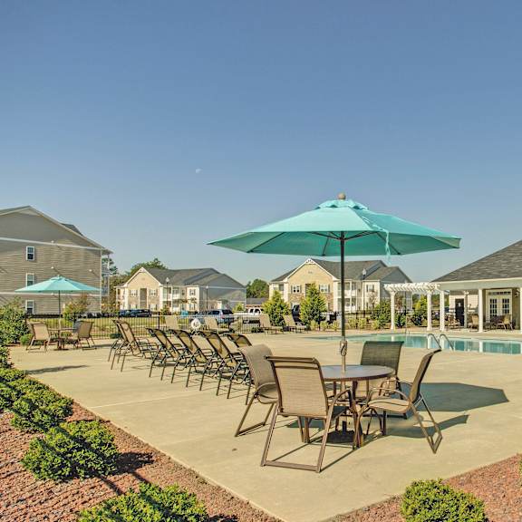 a patio with chairs and umbrellas overlooking a pool.