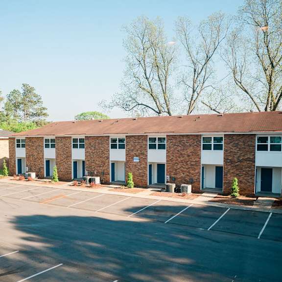 a parking lot in front of a brick building with trees in the background.