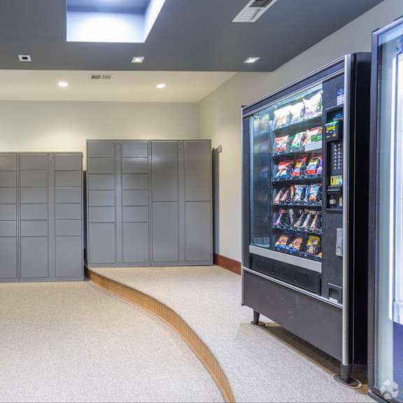 a vending machine is on the right side of a room with grey lockers.