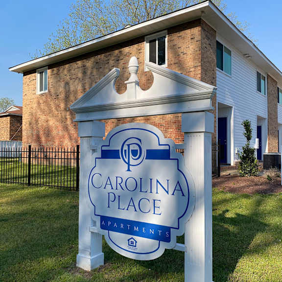 a sign for carolina place apartments stands in front of a brick building.