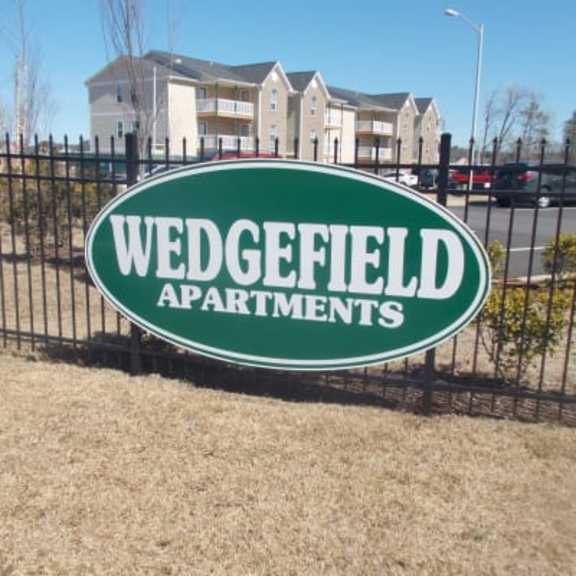 a sign for wedgefield apartments is shown in front of a fence and some grass.