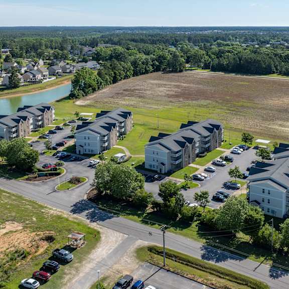 a bird's eye view of a residential area with apartment buildings, a parking lot, and a water body.