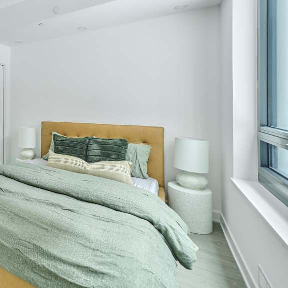 a bedroom with white walls and a bed with grey blankets and pillows