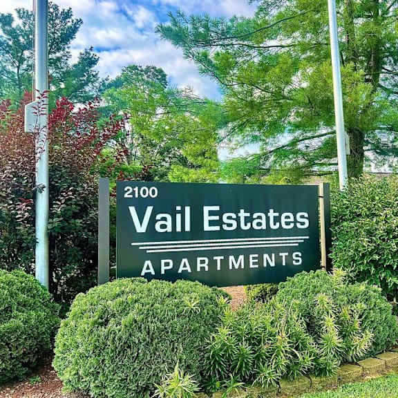 a sign for vail estates apartments is surrounded by green bushes.