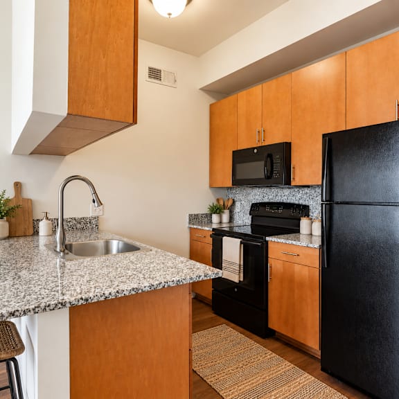 a black refrigerator sits in a kitchen with wooden cabinets and a granite countertop.