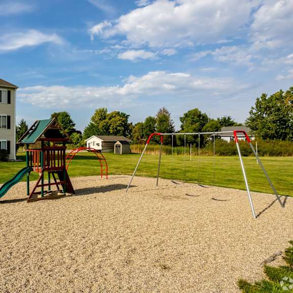 a playground with a green slide and a red swing set in front of a building.