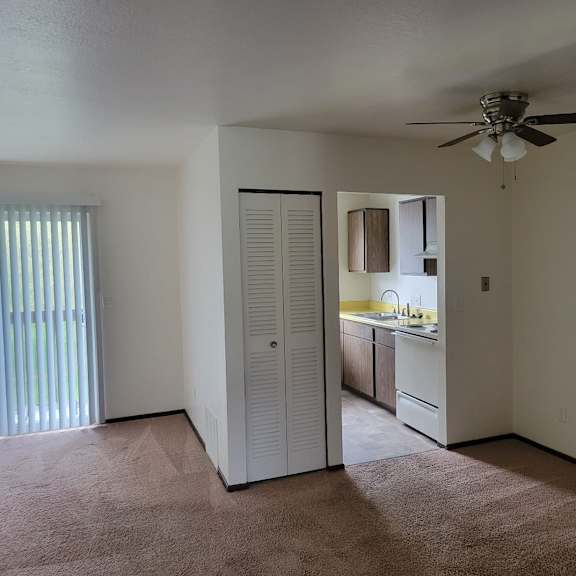 an empty living room with a ceiling fan and a kitchen