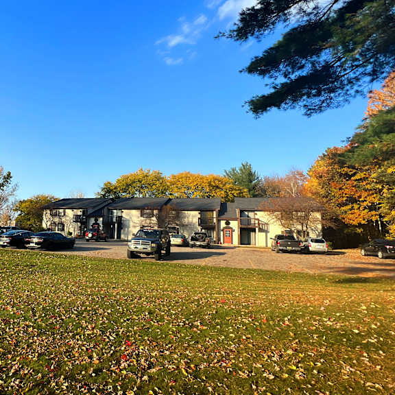 a house in the middle of a grassy field with cars parked in front of it