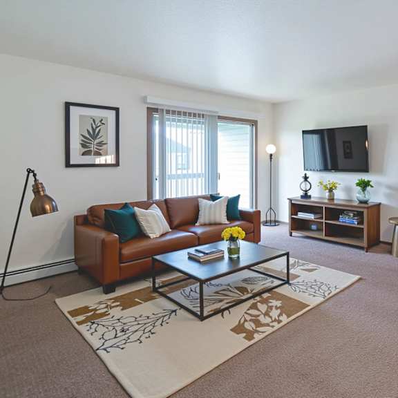 a living room with a brown couch, a coffee table, and a flat screen tv mounted on the wall.