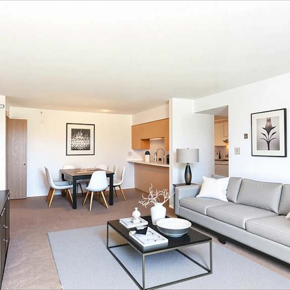 a modern living room with a grey couch, a glass coffee table, and a dining table with chairs.