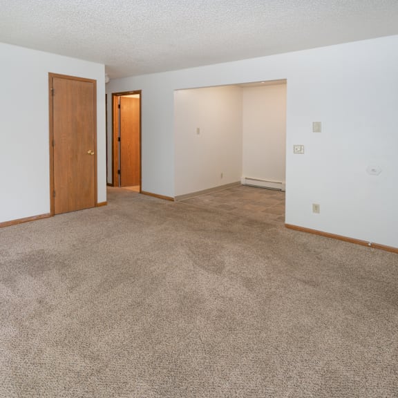 an empty living room with carpet and a door to a bedroom