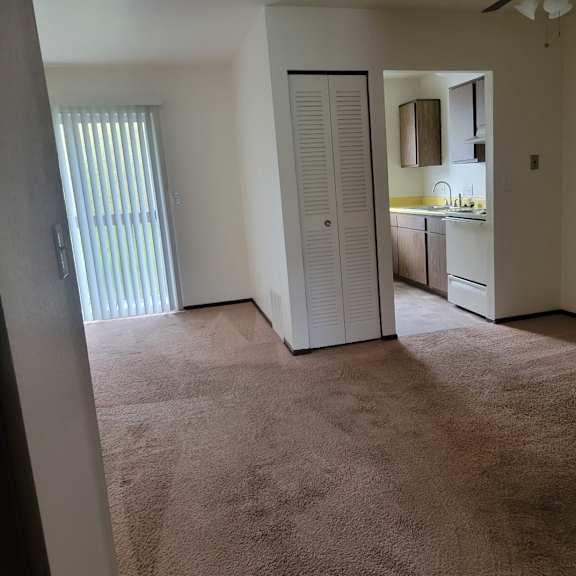 an empty living room with a door to a kitchen
