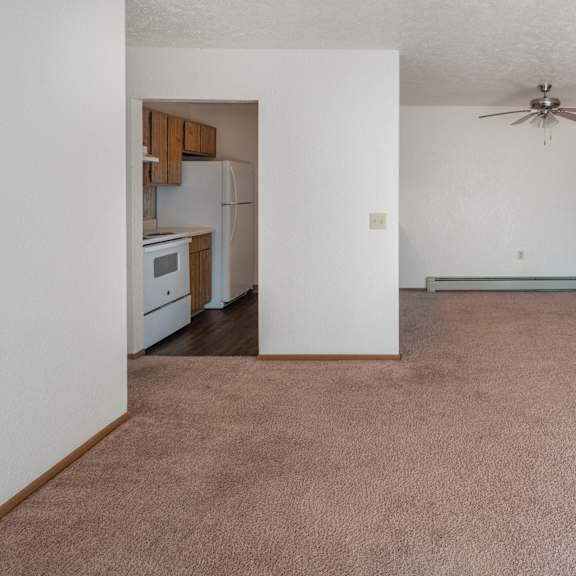 an empty living room with a ceiling fan and a kitchen