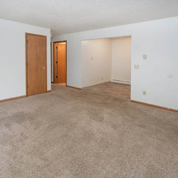 an empty living room with carpet and a door to a bedroom