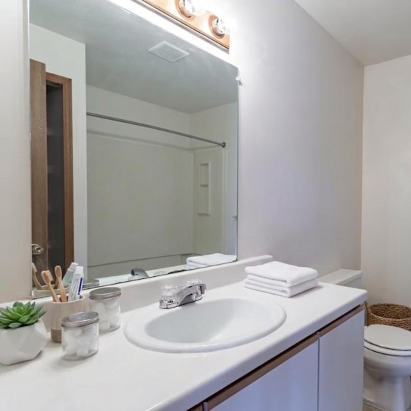 a white bathroom with a sink, mirror, toilet and a towel.