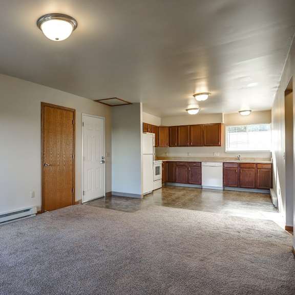 an empty living room with a kitchen in the background