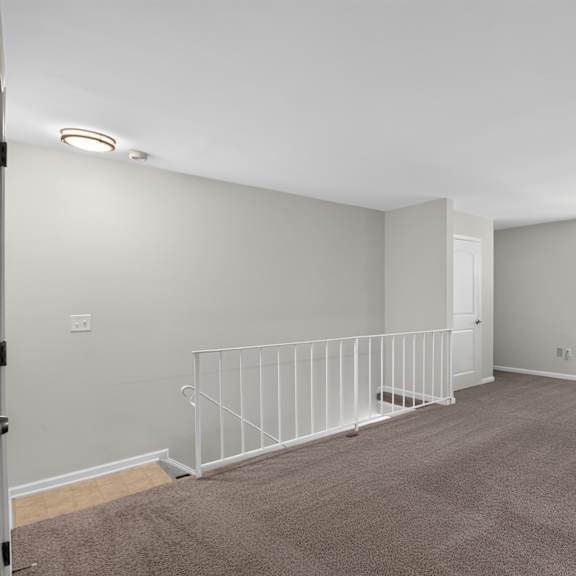 a sparsely furnished room with a carpeted floor and white railings.