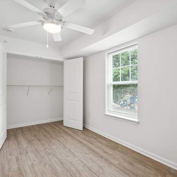 a room with a ceiling fan and a window showing trees outside.
