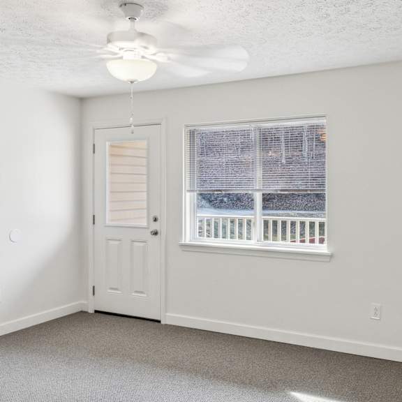 a room with a ceiling fan and a window overlooking a balcony.