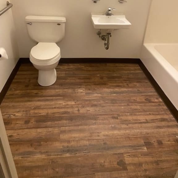 a white toilet sits in a bathroom with a wooden floor.