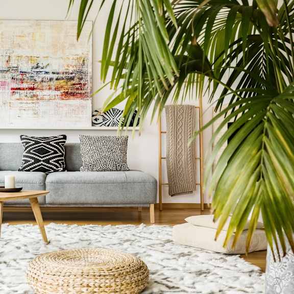 a living room with a grey couch, a woven stool, and a large abstract painting on the wall.