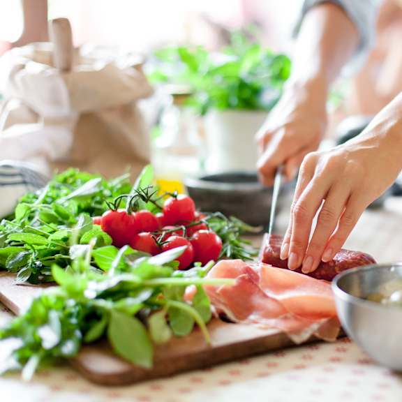 a woman cutting meat on a cutting board with vegetables on a table