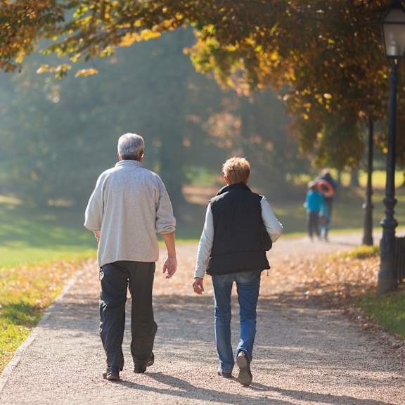 an older couple walking down a path in a park