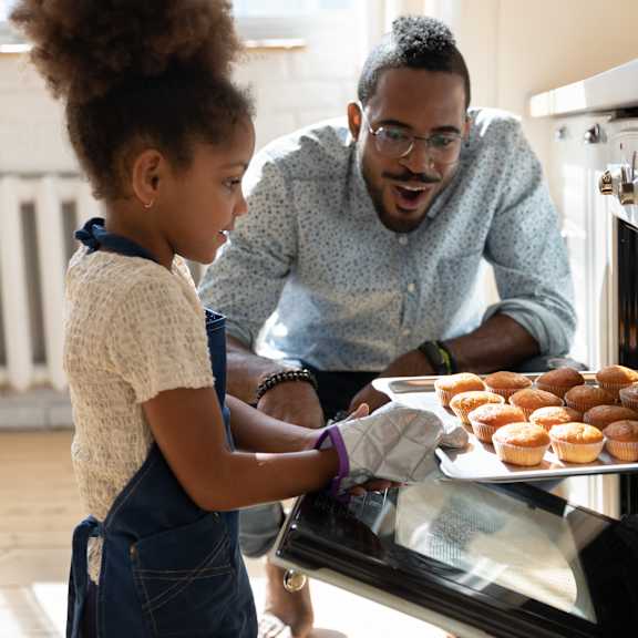 a father and daughter putting a tray of donuts into an oven
