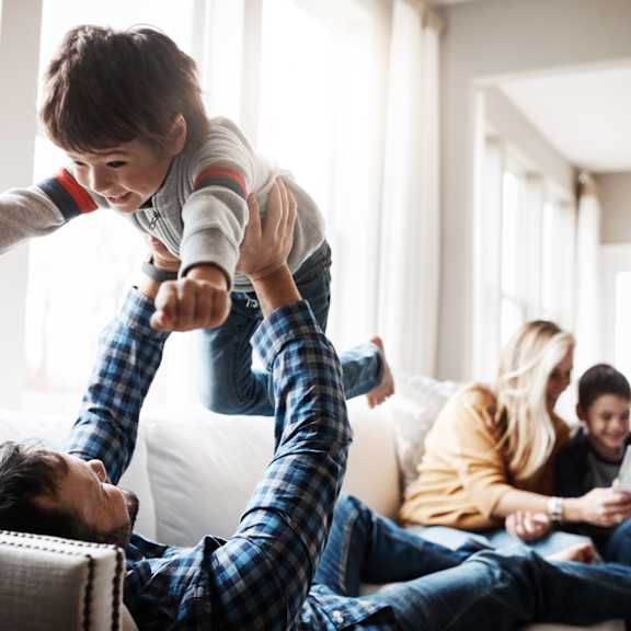 a young boy jumping on a man in the living room with his family