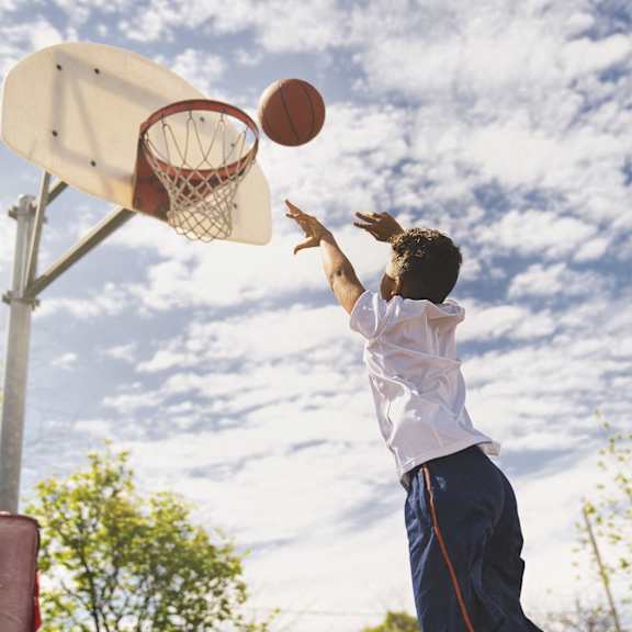 a boy in a white shirt and blue shorts is shooting a basketball into a hoop.