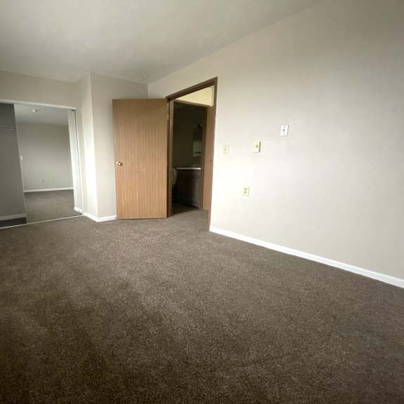an empty living room with carpet and a door into a bedroom
