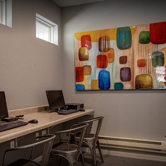 a study room with two computers and a painting on the wall