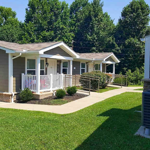 a small gray house with a porch and a yard with a lawn and trees