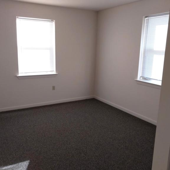 a room with a carpeted floor and two windows.